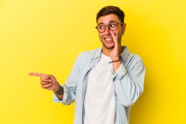 Sarı arka planda dövmeleri olan beyaz bir genç adam dedikodu yapıyor, bir şeyleri haber veriyor..