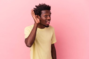 Genç Afrikalı Amerikalı bir adam pembe arka planda izole edilmiş bir şekilde bir dedikoduyu dinlemeye çalışıyor..