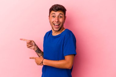 Sarı arka planda izole edilmiş beyaz dövmeli genç bir adam işaret parmağıyla işaret ederek heyecanlanıyor..