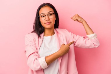 Pembe arka planda izole edilmiş genç Latin kadın güçlü bir hareket gösteriyor, kollarıyla, kadınsı gücün sembolü.