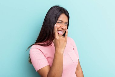 Genç Venezuelalı kadın mavi arka planda izole edilmiş. Parmaklarıyla kaya hareketi gösteriyor.