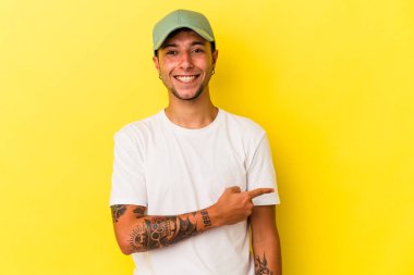 Sarı arka planda izole edilmiş, gülümseyen ve işaret eden, boş alanda bir şeyler gösteren beyaz dövmeli genç bir adam..