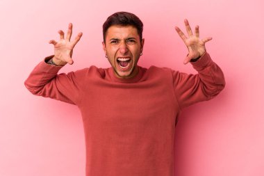 Sarı arka planda, pençelerini kedi taklidi yaparken gösteren dövmeleri olan genç beyaz bir adam. Saldırgan bir hareket..