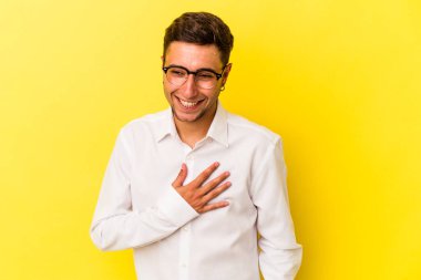 Sarı arka planda izole edilmiş dövmeleri olan genç beyaz bir adam gülüyor, ellerini yüreğine koyuyor, mutluluk kavramını koruyor..