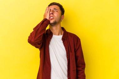 Sarı arka planda izole edilmiş dövmeleri olan genç beyaz bir adam yorgun ve uykulu bir şekilde ellerini başının üstünde tutuyor..