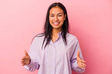 Pembe arka planda izole edilmiş genç Latin kadın iki eliyle bir şey tutuyor, ürün sunumu..