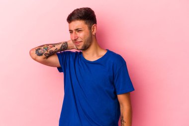 Sarı arka planda dövmeleri olan genç, beyaz bir adam stresten dolayı boynu ağrıyor, masaj yapıyor ve ona eliyle dokunuyor..