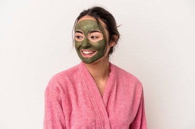 Young caucasian woman wearing a facial mask isolated on white background looks aside smiling, cheerful and pleasant.