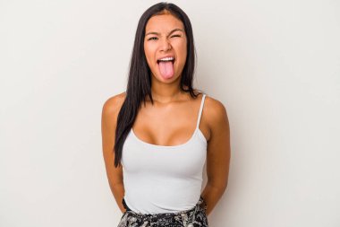 Beyaz arka planda izole edilmiş genç Latin bir kadın. Komik ve dost canlısı bir dil uzatıyor..