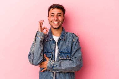 Sarı arka planda izole edilmiş dövmeleri olan beyaz bir genç göz kırpıyor ve elleriyle iyi bir jest yapıyor..