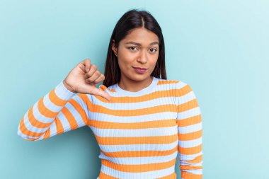 Genç Venezuelalı bir kadın mavi arka planda izole edilmiş, hoşlanmadığı bir jest gösteriyor, başparmakları aşağıda. Anlaşmazlık konsepti.