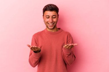 Sarı arka planda izole edilmiş beyaz dövmeli genç bir adam avuçlarıyla bir şey tutuyor ve kameraya sunuyor..