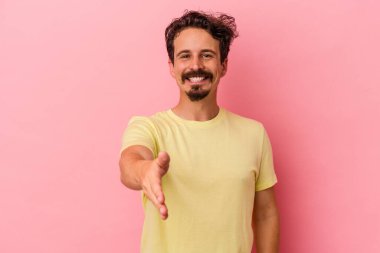 Pembe arka planda izole edilmiş genç beyaz adam selamlama jesti olarak kameraya elini uzatıyor..