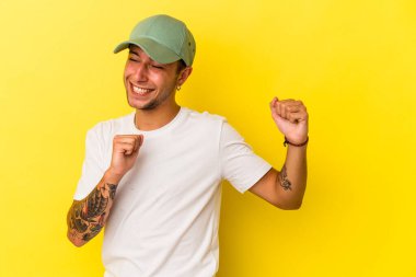 Sarı arka planda izole edilmiş dövmeleri olan genç beyaz adam dans ediyor ve eğleniyor..