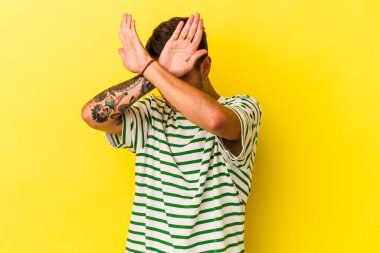 Sarı arka planda izole edilmiş, iki kolu çapraz tutan, inkar kavramı olan beyaz dövmeli genç bir adam..