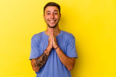 Sarı arka planda izole edilmiş, ağzı yakınında dua eden, kendine güvenen beyaz dövmeli genç bir adam..