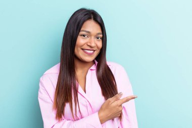 Genç Venezuelalı bir kadın mavi arka planda izole edilmiş gülümseyen ve işaret eden boş uzayda bir şey gösteriyor..