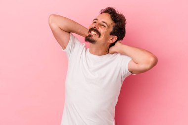 Pembe arka planda izole edilmiş genç beyaz bir adam kendini güvende hissediyor, elleri başının arkasında..
