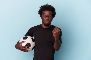 Amerikan futbolu oynayan genç Afro-Amerikalı adam mavi arka planda izole edilmiş kameraya yumruk gösteriyor, agresif yüz ifadesi var..