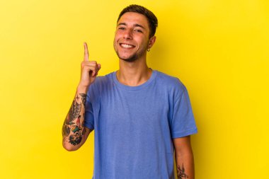 Sarı arka planda dövmeleri olan genç beyaz bir adam bir numarayı parmağıyla gösteriyor..