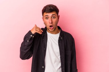 Sarı arka planda izole edilmiş dövmeleri olan genç beyaz bir adam bir şeye gülüyor, elleri ağızda..