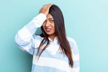 Genç Venezuelalı bir kadın mavi arka planda izole edilmiş bir şekilde bir şeyi unutuyor. Alnına avuç içi ve kapalı gözlerle vuruyor..