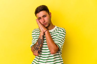 Sarı arka planda izole edilmiş dövmeleri olan genç, beyaz bir adam esneyerek ağzını eliyle kapatan yorgun bir jest yapıyor..
