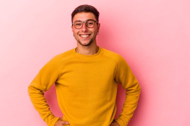 Sarı arka planda izole edilmiş dövmeleri olan genç, beyaz bir adam ellerini kalçasında tutuyor..