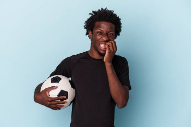Amerikan futbolu oynayan genç Afrikalı bir adam mavi arka planda izole edilmiş tırnak yiyor, gergin ve çok endişeli..