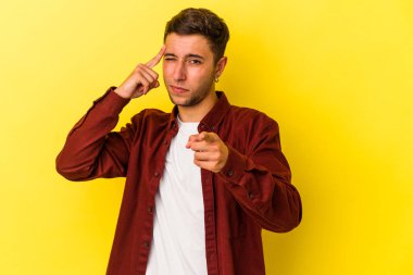 Sarı arka planda izole edilmiş beyaz dövmeli genç bir adam şakağı parmağıyla işaret ediyor, düşünüyor ve bir göreve odaklanıyor..