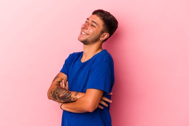 Sarı arka planda izole edilmiş dövmeleri olan genç beyaz adam kollarını kavuşturarak gülümsüyor..