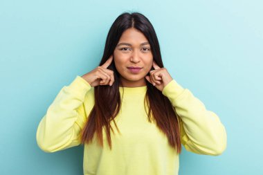 Genç Venezuelalı bir kadın mavi arka planda izole edilmiş parmaklarıyla kulaklarını kapatıyor, gürültülü bir ortam yüzünden stresli ve çaresiz..