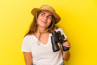 Dürbün tutan genç beyaz kadın sarı arka planda izole edilmiş hedeflere ve amaçlara ulaşma hayali kuruyor.