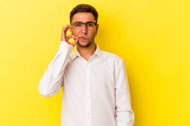 Sarı arka planda dövmeleri olan genç beyaz bir adam. Parmakları dudaklarında bir sır saklıyor..