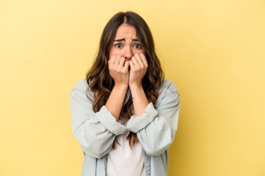 Sarı arka planda izole edilmiş, tırnak yiyen, gergin ve endişeli bir beyaz kadın..