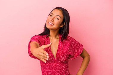 Pembe arka planda izole edilmiş genç Latin kadın selamlaşma jesti olarak kameraya uzanıyor..