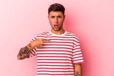 Sarı arka planda izole edilmiş beyaz dövmeli genç bir adam parmağıyla işaret ederek şaşırdı, geniş bir gülümsemeyle..