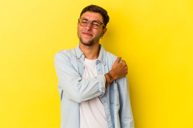 Sarı arka planda izole edilmiş, omuz ağrısı olan beyaz dövmeli genç bir adam..