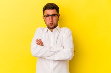 Sarı arka planda izole edilmiş dövmeleri olan beyaz genç bir adam omuzlarını silker ve gözleri açık kalır..