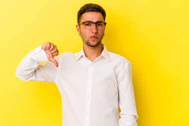 Sarı arka planda izole edilmiş beyaz dövmeli genç bir adam baş parmağını aşağı gösteriyor, hayal kırıklığı konsepti..