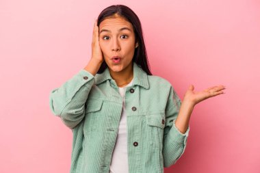 Pembe arka planda izole edilmiş genç Latin kadın, avuç içi fotokopi alanını tutmaktan etkilenmiş..