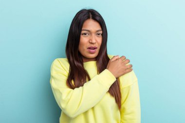 Genç Venezuelalı bir kadın mavi arka planda izole edilmiş, omuz ağrısı var..