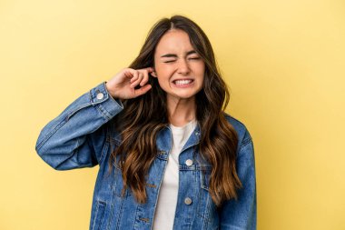 Sarı arka planda izole edilmiş genç beyaz bir kadın parmaklarıyla kulaklarını kapatıyor, gürültülü bir ortam yüzünden stresli ve çaresiz..