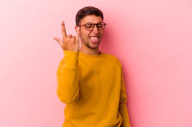 Sarı arka planda izole edilmiş dövmeleri olan genç beyaz bir adam parmaklarıyla taş hareketi gösteriyor.