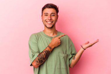 Sarı arka planda izole edilmiş dövmeleri olan genç beyaz bir adam, palmiye ağacında bir kopya alanı tutarken heyecanlanıyor..