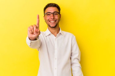 Sarı arka planda dövmeleri olan genç beyaz bir adam bir numarayı parmağıyla gösteriyor..