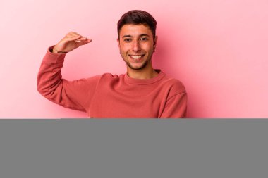 Sarı arka planda izole edilmiş beyaz dövmeli genç bir adam işaret parmaklarıyla küçük bir şey tutuyor, gülümsüyor ve kendinden emin..