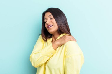 Genç Venezuelalı bir kadın mavi arka planda izole edilmiş, omuz ağrısı var..