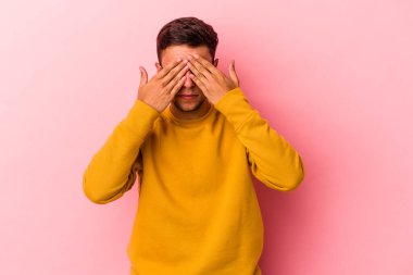 Sarı arka planda izole edilmiş dövmeleri olan genç beyaz bir adam elleriyle gözlerini kapatmaktan korkuyor..