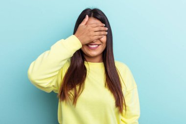 Genç Venezüellalı bir kadın mavi arka planda soyutlanmış, elleriyle gözlerini kapatmış, gülümseyerek bir sürpriz bekliyor..